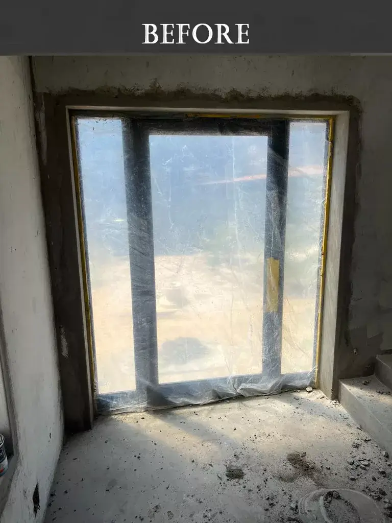 Unfinished window during home renovation, covered with protective plastic sheeting and surrounded by rough concrete walls and construction debris.