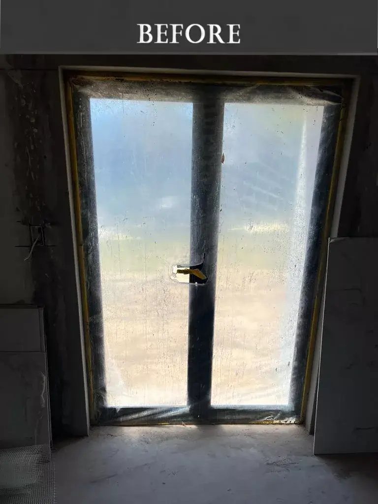 Dust-covered window with plastic sheeting in a room under renovation, showing unfinished walls and construction materials nearby. Unfinished window during home renovation, covered with protective plastic sheeting and surrounded by rough concrete walls and construction debris.